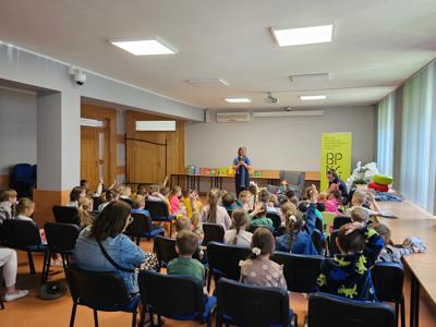 Na zdjęicu duża grupa dzieci siedzaca na krzesłach na duzej sali