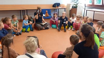 Na zdjęciu grupa dzieci siedząca w kółku i patrząca na kobietę