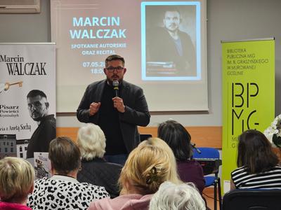 Na zdjęciu młody mężczyzna trzymajacy mikrofon i pzremawiajacy do ludzi