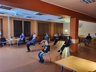 ludzie siedzący w dużej odległości od siebie na krzesełkach w maseczkach