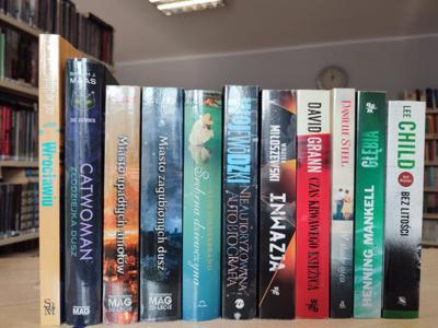 ksiązki leżące z widocznymi grzbietami , w tle regały biblioteczne z ksiązkami