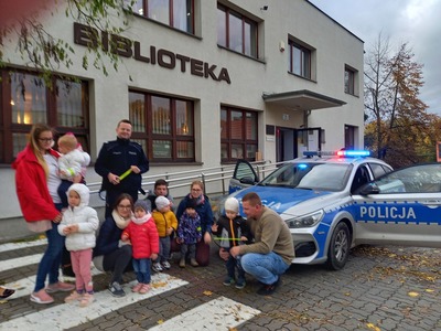 Grupa dzieci stojąca wraz z policjantem przy radiowozie policyjnym