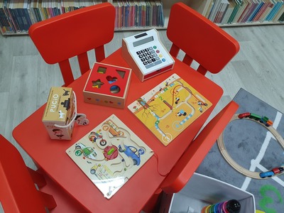 Czerwony stolik  i czerwone krzesełka dla dzieci. Na nich ułożone zabawki edukacyjne