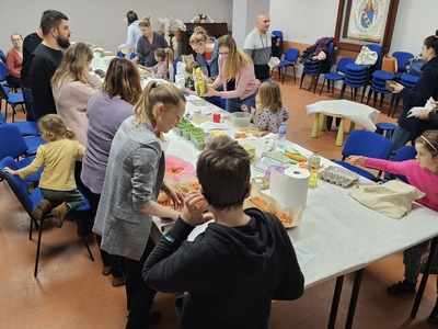 Grupa ludzi stojąca przy stolikach i krojąca warzywa i owoce