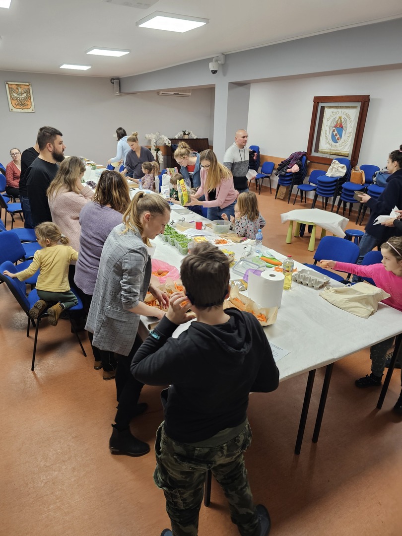 Grupa ludzi stojąca przy stolikach i krojąca warzywa i owoce