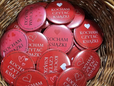 Na zdjęciu czerwone i różowe przypinki z białym napisem kocham czytać książki