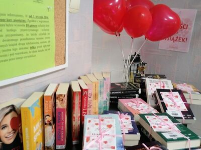 Na zdjęciu książki ułożone na komodzie, obok balony w kształcie serca