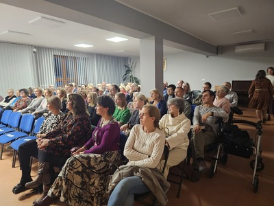 Duża grupa ludzi siedzących na krzesłach na sali i patrzących w jedną stronę