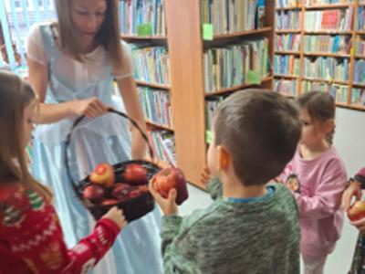 Kobieta w błękitnej sukni rozdająca jabłka dzieciom