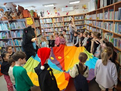 dzieci oraz duzy czarny kto trzymający kolorową chustę animacyjną w bibliotece