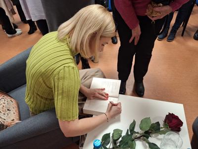 autorka książek podpisuje książkę na białym stoliku, obok lezy czerwona róża