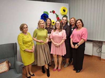 kobiety stojące razem, obok fotel oraz tło z kwiatami