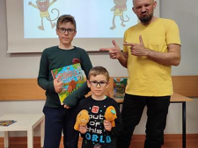 dwoje dzieci, jedno trzyma ksiązkę, drugie maskotki stoją obok mężczyzny w żółtej koszulce w tle obraz na rzutniku