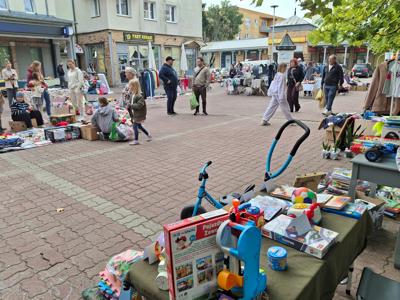 rynek w mieście, stoiska pchli targ, ludzie pomiedzy nimi, na stoiskach zabawki, ubrania, rowerki