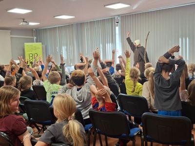 uczniowie trzeciej klasy podnoszący ręce przed dorosłym mężczyzną przebranym za wędrowca