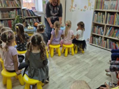 dzieci siedzące na żółtych tabroetach przed nimi dorosła kobieta
