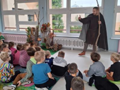 męzczyzna przebrany za pradawnego wędrowca opowiadający dzieciom siedzącym na dywanie legendy