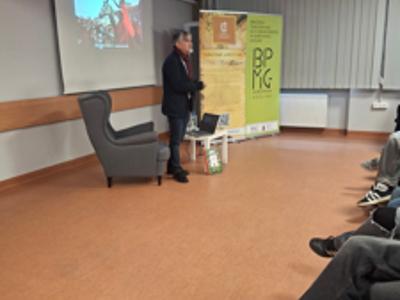 mężczyzna stojący przy fotelu, wypowiadający się do młodzieży