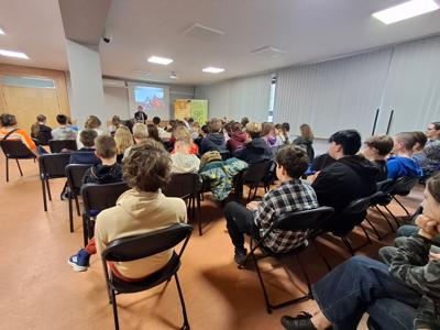 uczniowie siedzący na krzesełkach przodem do wykładowcy