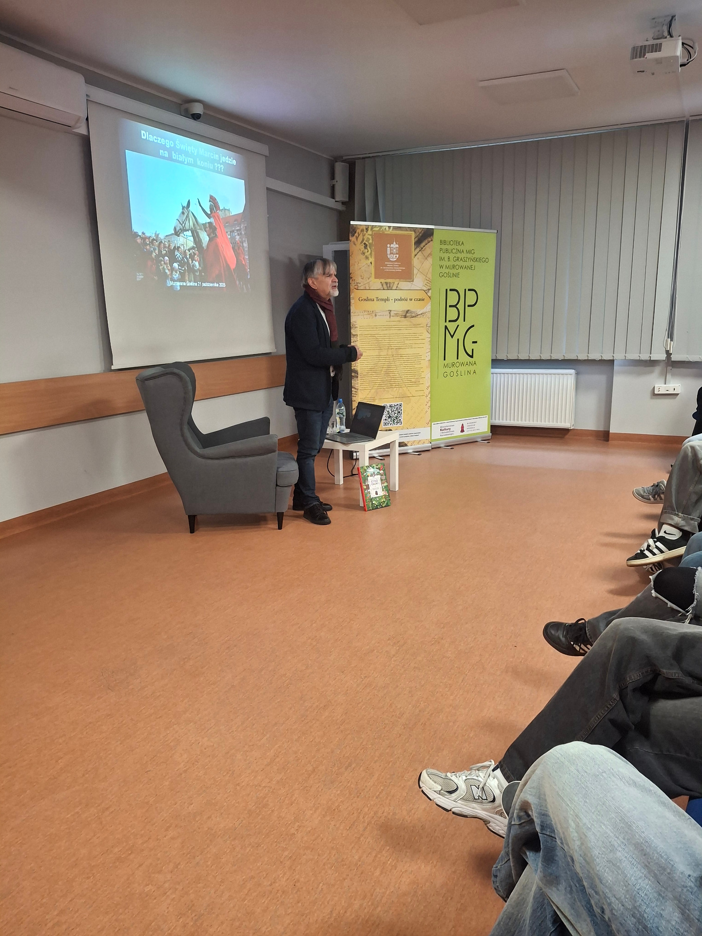 mężczyzna stojący przy fotelu, wypowiadający się do młodzieży 