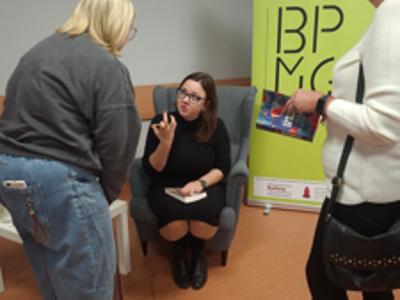 kobieta na fotelu podpsiuje książkę, przed nią dwie kobiety