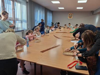 osoby siedzące przy dużym stole i wyplatające wikline