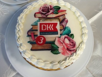 Tort z grafiką w postaci książek, kwiatów i logo DKK