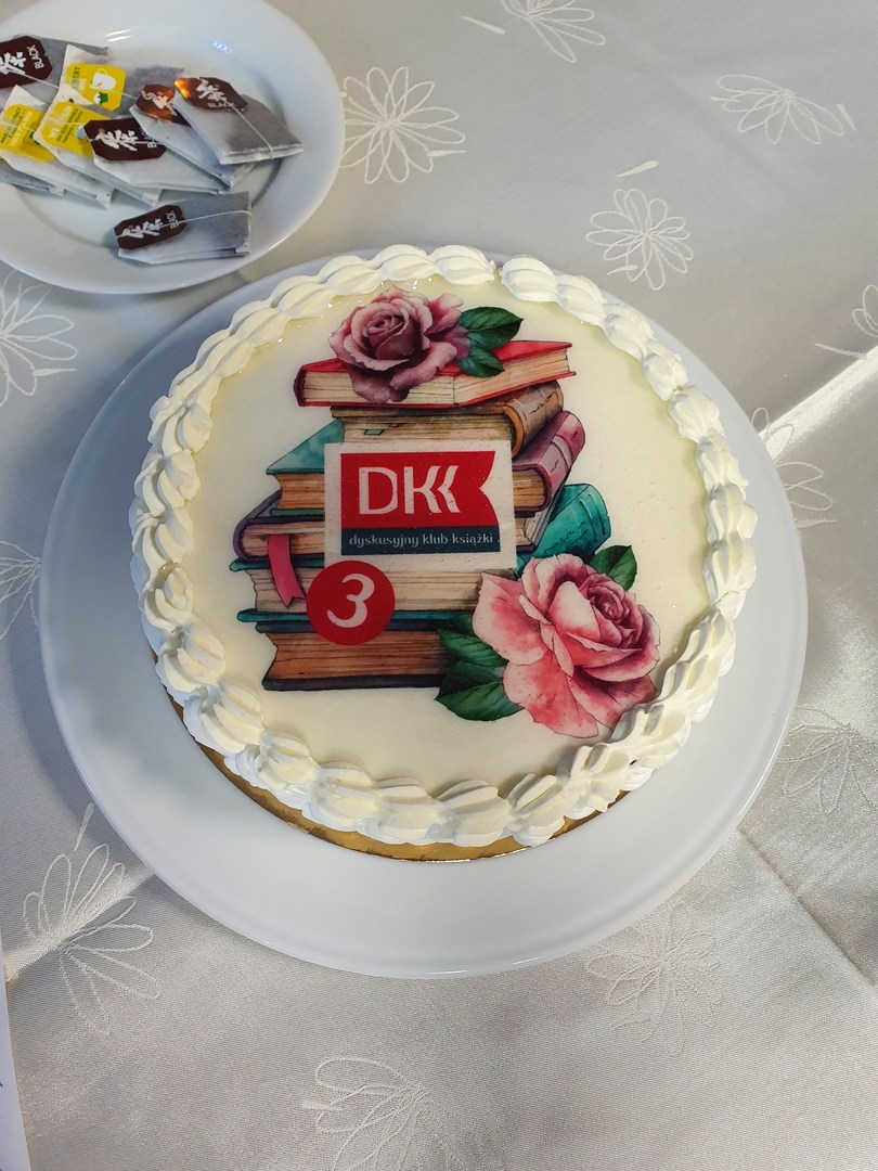 Tort z grafiką w postaci książek, kwiatów i logo DKK