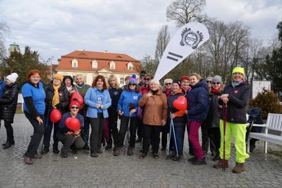 Grupa starszych osób na tle budynku sądu w Żaganiu z banerem : "Stowarzyszenie Turystyczne Piechur".