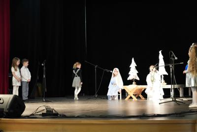 Grupa dziecięca przedstawiająca jasełka na scenie. Dziewczynka podchodzi do mikrofonu.
