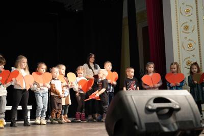 Dzieci trzymają w rękach papierowe serduszka na scenie.