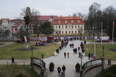 Widok przed Pałacem Książęcym - ludzie, karetka, pojazd strażacki, karuzela. W tle widać budynki miejskie.