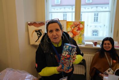 Pani trzyma puszkę WOŚP. Za nią obrazy i okno.