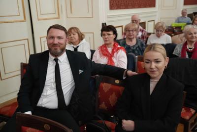 Ludzie siedzący na widowni. Na pierwszym planie elegancko ubrane, uśmiechnięte osoby.