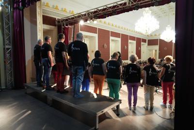 Grupa ludzi na scenie, występ chóru. W tle publiczność.