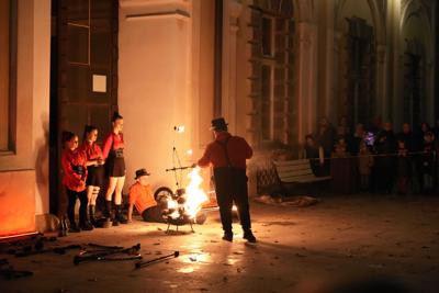 Ciemno, scenę rozjaśnia ogień - grupa ludzi przygotowuje się do występu z ogniem.