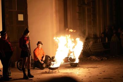 Jest ciemno, widać żarzące się kije do występów z ogniem, w tle siedzą występujący.