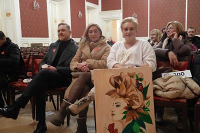 Grupa osób siedząca na widowni. Na pierwszym planie pani siedzi trzymając obraz.