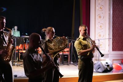 Trzy osoby grają na instrumentach przed sceną.