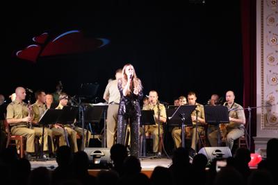 Dziewczyna śpiewa na scenie, za nią orkiestra wojskowa.