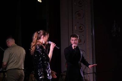 Pan śpiewa z panią na scenie. Za nimi dyrygent orkiestry wojskowej.