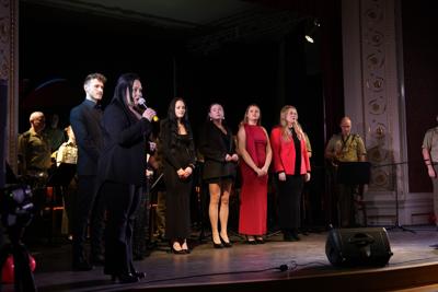 Pani przemawia do publiczności, za nią artyści i orkiestra wojskowa.
