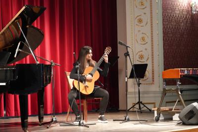 Dziewczyna gra na gitarze na scenie. Wokół stoją inne instrumenty.