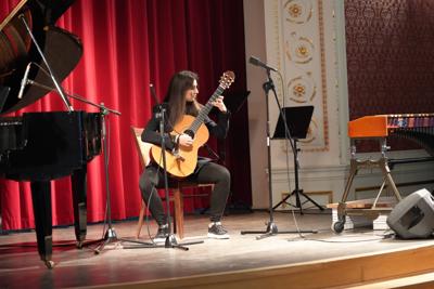 Dziewczyna gra na gitarze na scenie. Wokół stoją inne instrumenty.