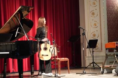 Dziewczyna stoi z gitarą na scenie. Wokół stoją inne instrumenty.