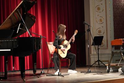 Dziewczyna gra na gitarze na scenie. Wokół stoją inne instrumenty.
