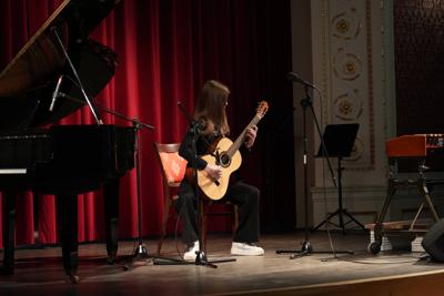 Dziewczyna gra na gitarze na scenie. Wokół stoją inne instrumenty.