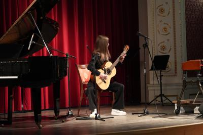 Dziewczyna gra na gitarze na scenie. Wokół stoją inne instrumenty.