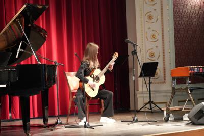 Dziewczyna gra na gitarze na scenie. Wokół stoją inne instrumenty.