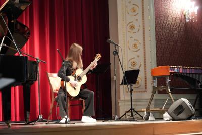 Dziewczyna gra na gitarze na scenie. Wokół stoją inne instrumenty.